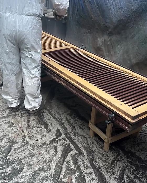 Operatore in tuta protettiva accanto a persiane a lamelle in legno durante la verniciatura